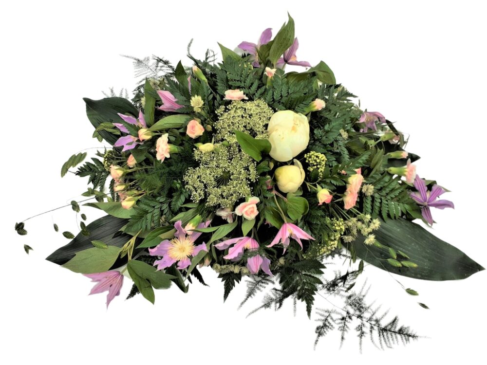 Låg begravningsdekoration i ljusa färger med bl.a. pion, elegansnejlika, kvistros, klematis hos Bellis blomsterhandel.
