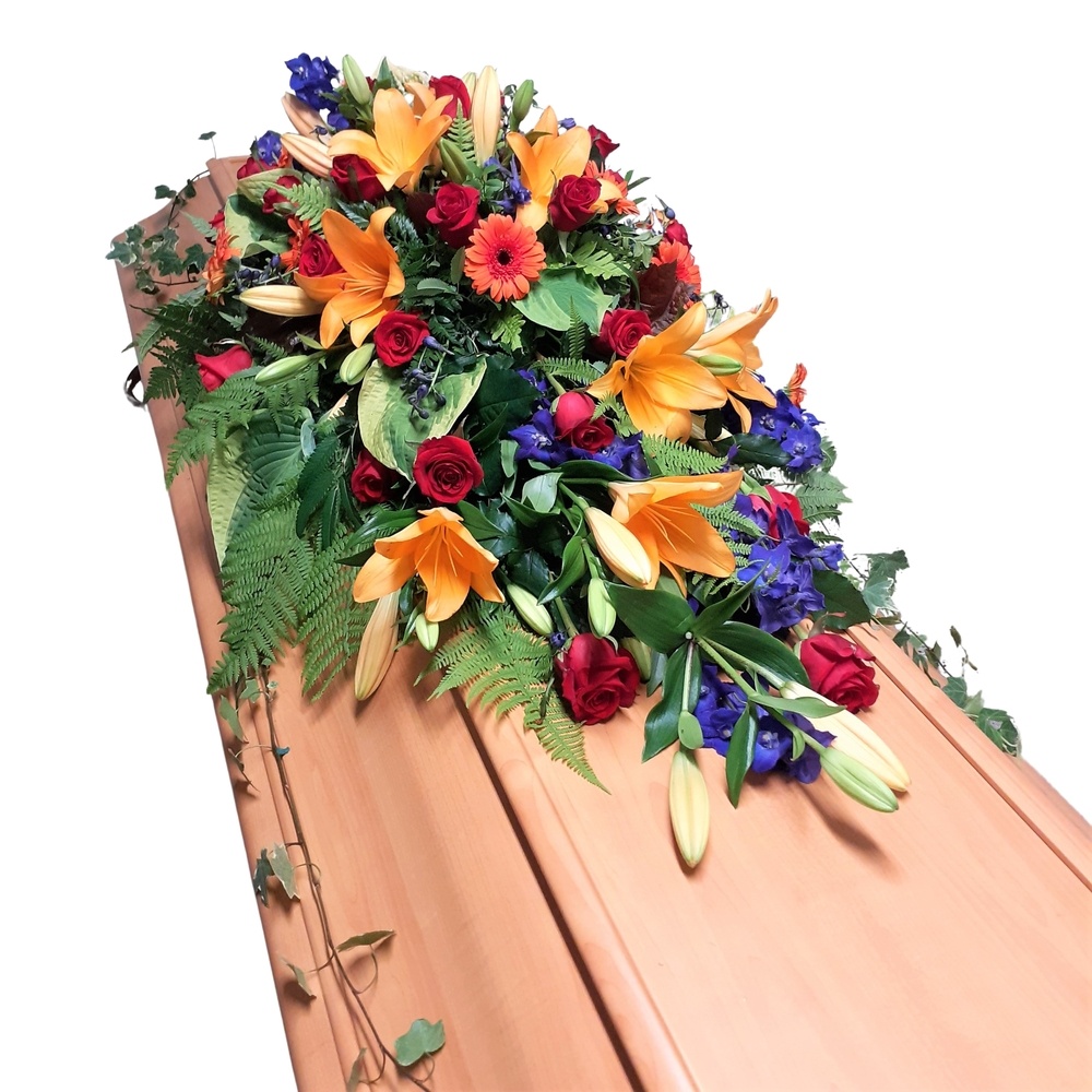 Kistdekoration i praktfulla färger innehållandes rosor, germini, lilja m.m. hos Bellis blomsterhandel.